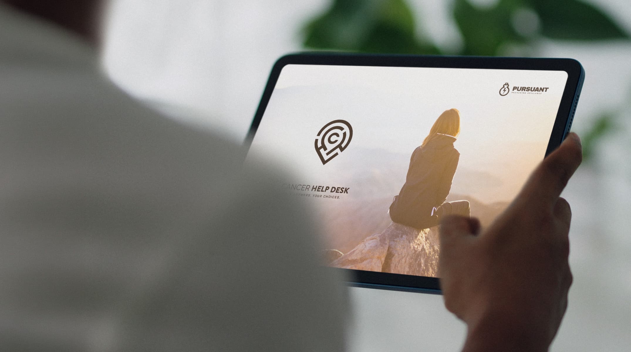 Tablet device showing Cancer Helpdesk brand concept with logo and image of a person sitting peacefully on a mountaintop.